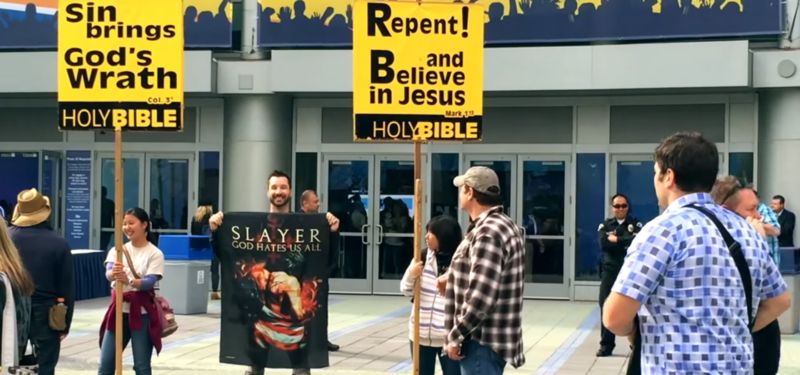 Flaga Slayera „Bóg nienawidzi nas wszystkich” obok demonstrantów religijnych