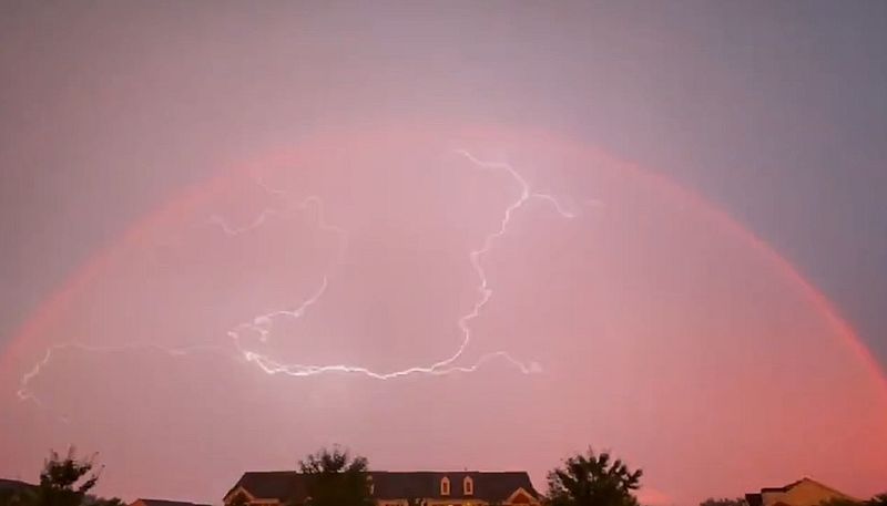 Doppelter Regenbogen bei Sonnenuntergang, in dessen Sphäre sich Blitze entladen